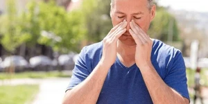 Man holding nose with both hands in discomfort